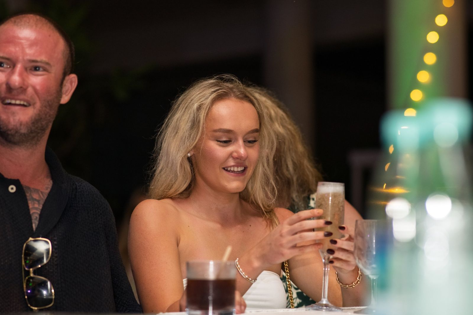 Guest smiling at her drink at a bar with fairy lights