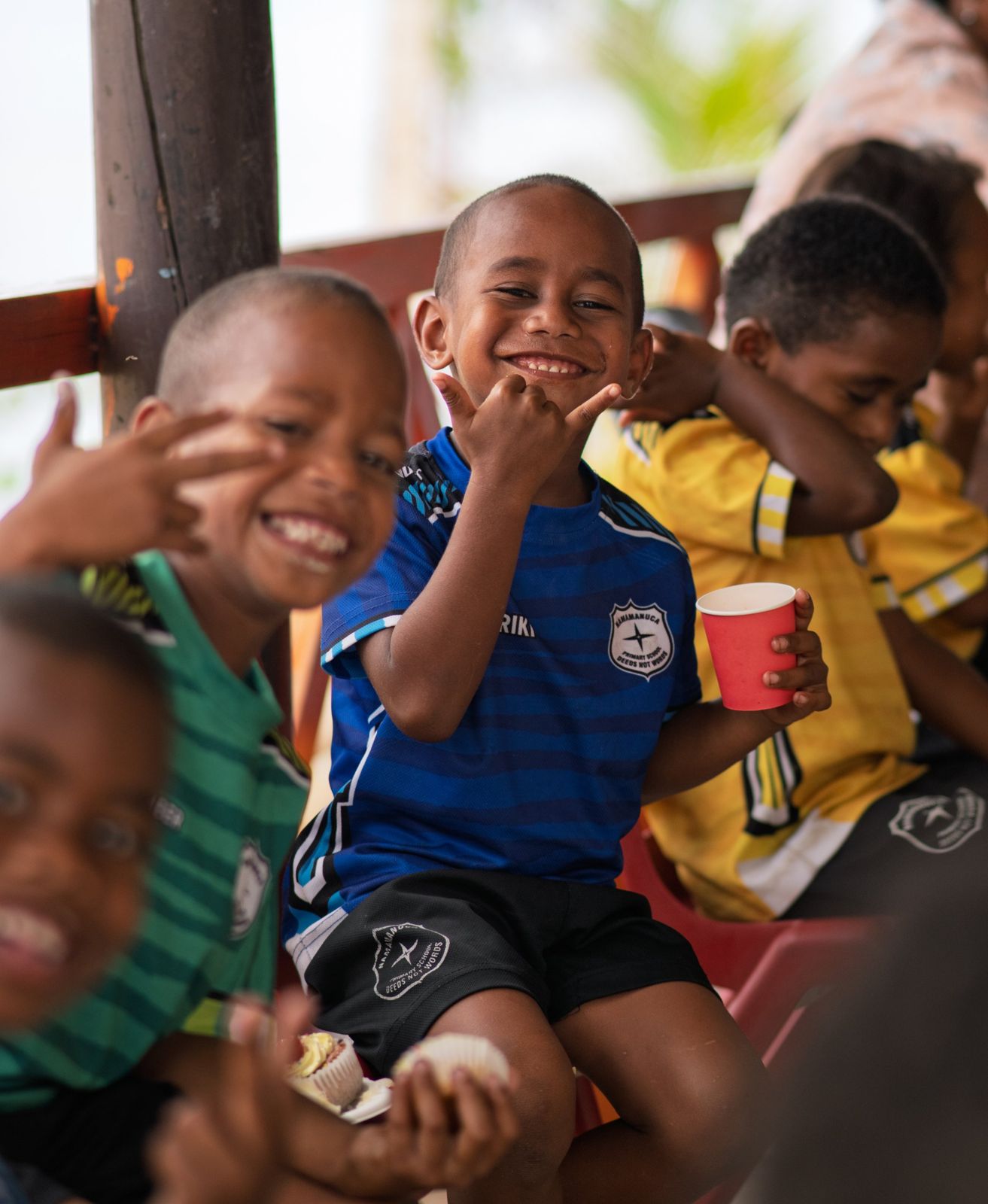 Boy in a blue school jersey smiling and giving a shaka