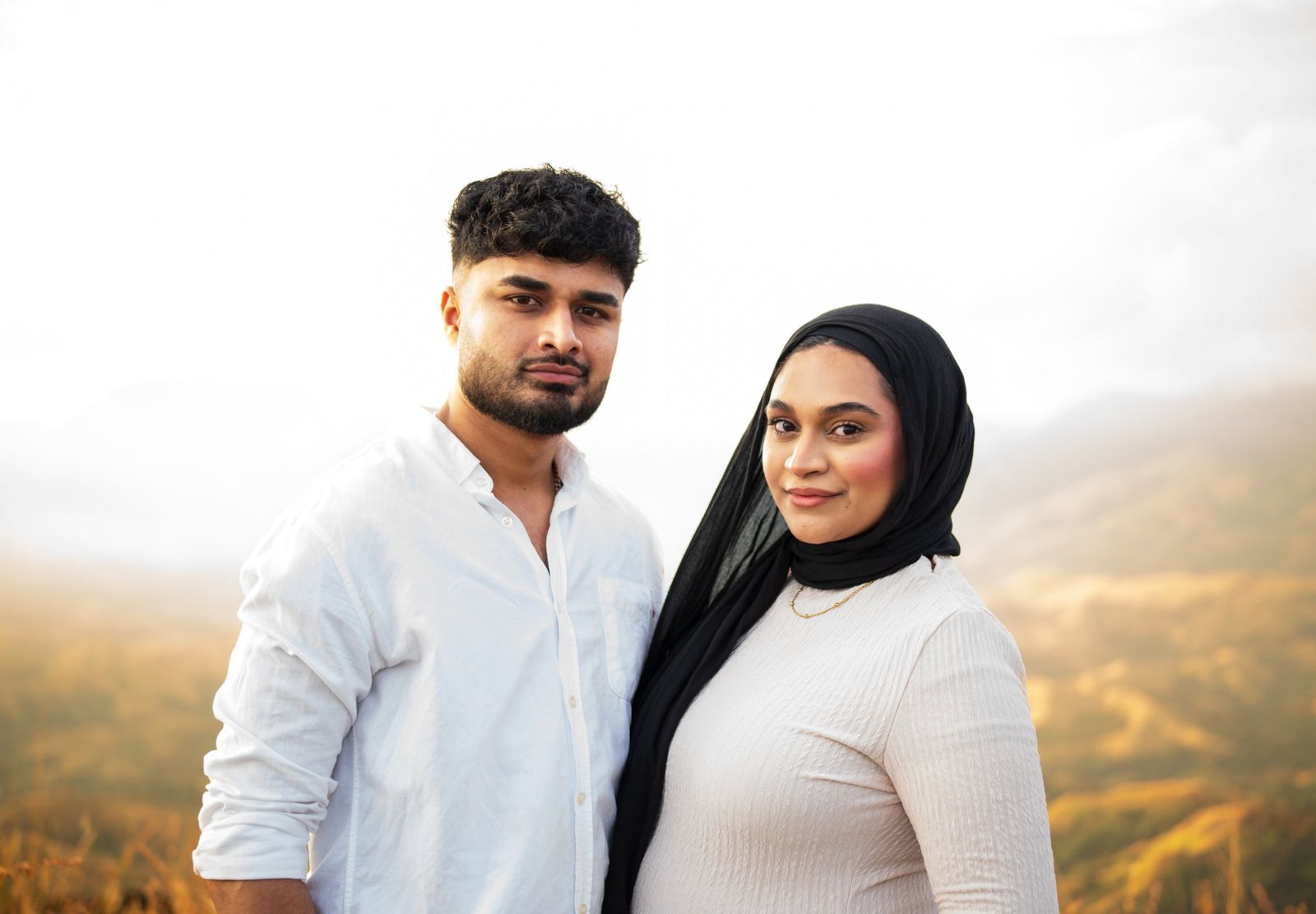 Couple standing close together with golden hills behind them