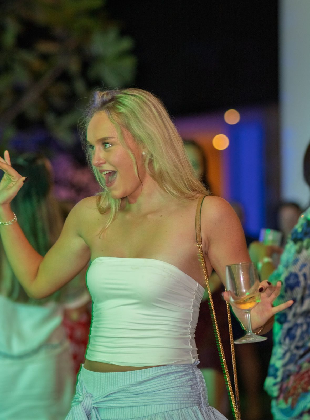 Woman dancing with a glass of wine under coloured lights