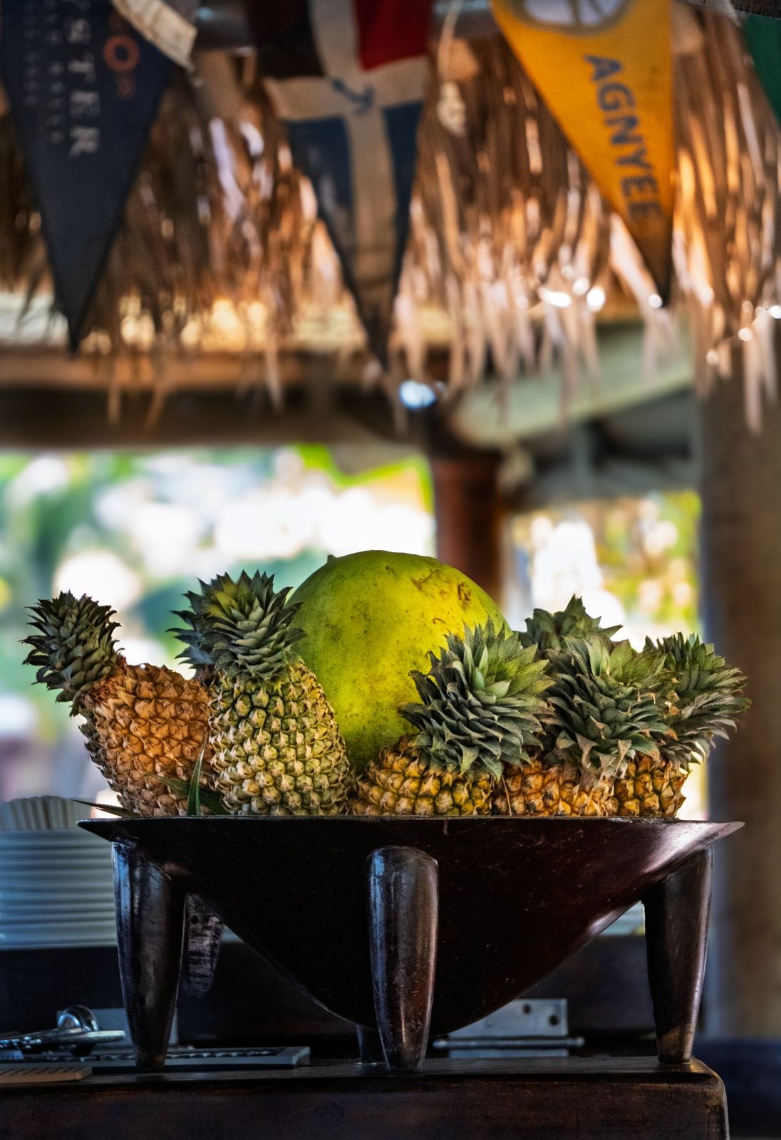 Pineapples and a coconut in a wooden kava bowl at a thatched bar