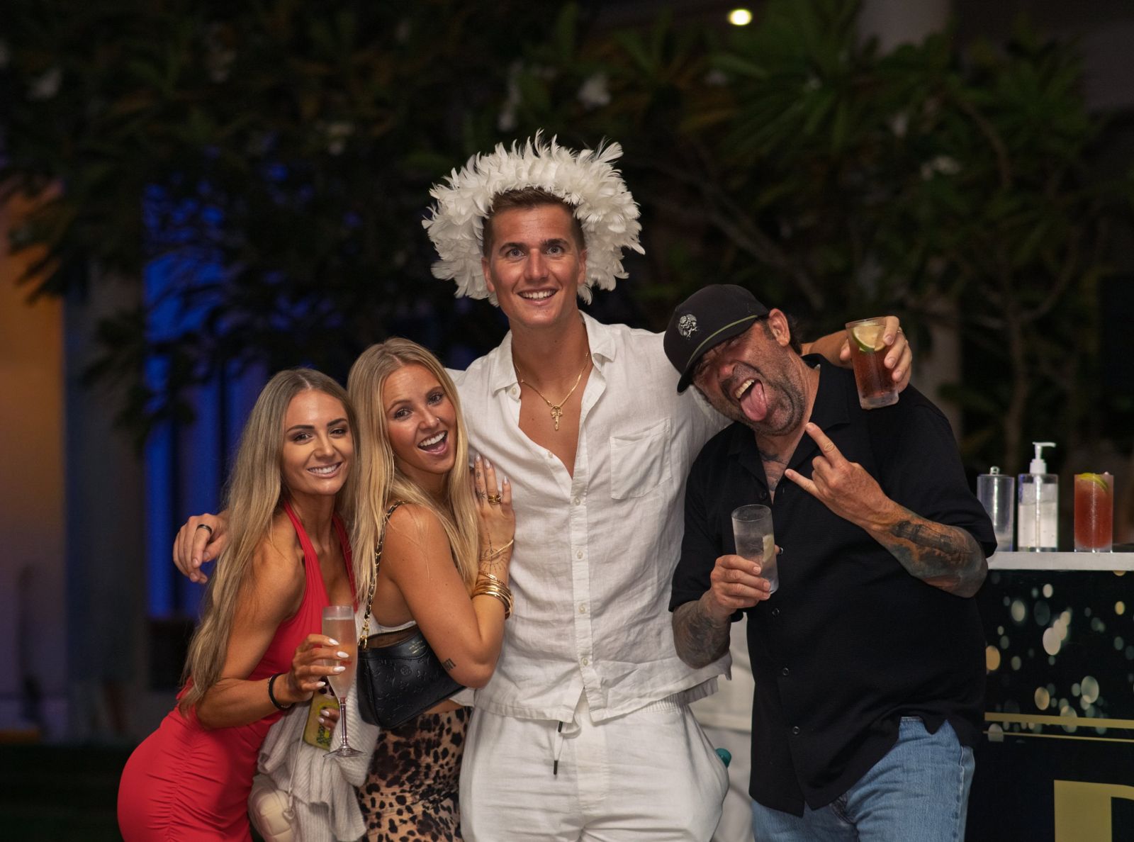 Four friends posing with drinks at a night party