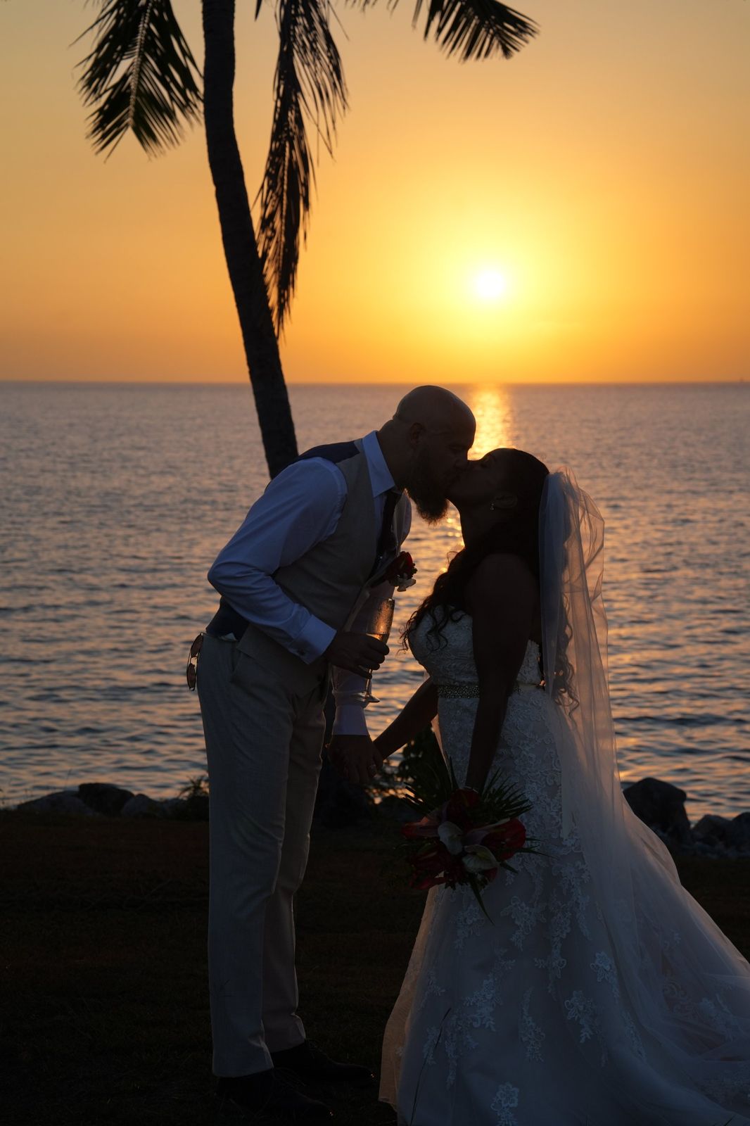 Bride and groom kissing in silhouette against an orange sunset over the sea